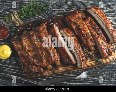 Schneiden gegrillte Schweinerippchen mit Sauce auf einem Brett, Gewürze, Holz- Hintergrund Stockfoto