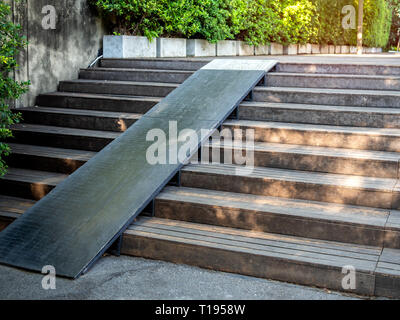 Plank Holz Treppe im Freien mit hölzernen Rollstuhl Rampe am grünen Baum Hintergrund. Alte hölzerne Treppe mit Holz- hang Weg in den Garten. Stockfoto