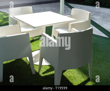 Weißes modernes Garten Esstisch mit vier Stühlen am grünen Hof. Sauberen, weißen Kunststoff Gartenmöbeln. Stockfoto