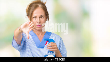 Mittleres Alter brunette Reiniger Frau tragen die Hausarbeit gleichmäßig über isolierte Hintergrund mit Verärgerten Gesicht, negatives Vorzeichen zeigen Abneigung mit Daumen nach unten, Stockfoto