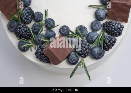 Frische und köstliche hausgemachte Kuchen mit Beeren, Schokolade und Rosmarin auf weißem Hintergrund, Ansicht von oben. Beeren und Rosmarin auf Kuchen. Geburtstag Kuchen close-up Stockfoto