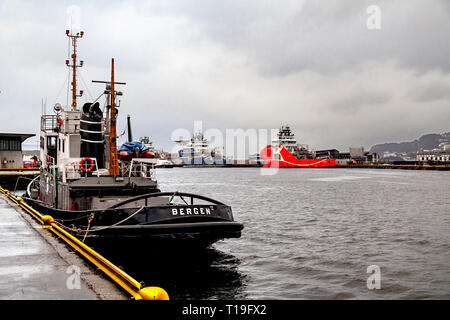 Veteran Tug Boat Vulcanus (erbaut 1959) im Hafen von Bergen, Norwegen Anker. An einem regnerischen Tag. Offshore-versorger im Hintergrund neben Skolten Quay. Stockfoto