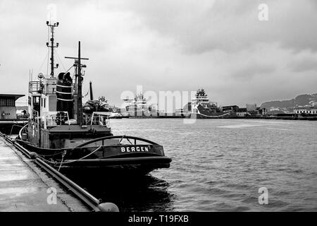 Veteran Tug Boat Vulcanus (erbaut 1959) im Hafen von Bergen, Norwegen Anker. An einem regnerischen Tag. Offshore-versorger im Hintergrund neben Skolten Quay. Stockfoto