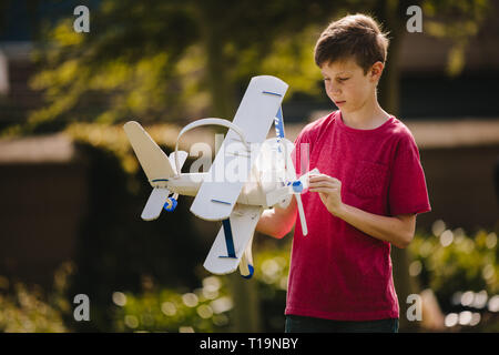 Junge spielt mit einem Spielzeug Flugzeug im Freien. Jugendliche junge Blick auf das Spielzeug Flugzeug in seine Hände im Freien. Stockfoto