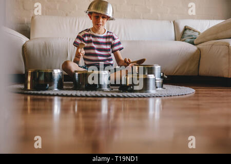 Wenig Musiker Schlagzeug spielen auf Küchenutensilien zu Hause. Unschuldige junge vorzugeben, ein Drummer sitzt auf dem Boden und Spielen auf Utensilien Stockfoto