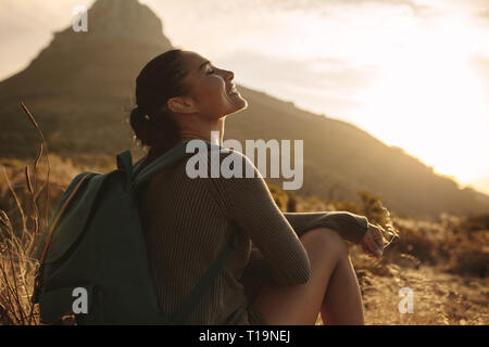 Frau sitzt auf dem Boden lächelnd mit geschlossenen Augen. Kaukasische weibliche Touristen eine Pause nach dem Wandern nach Land Trail. Stockfoto