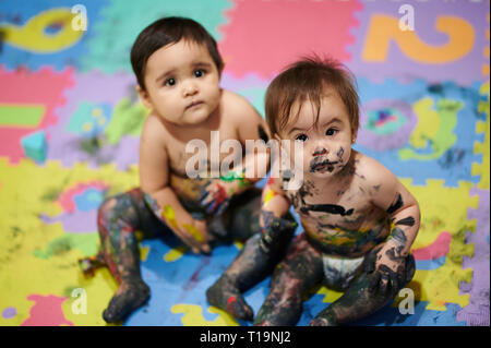 Bemalte Kinder sitzen auf bunten Hintergrund. Babys machen Chaos Stockfoto