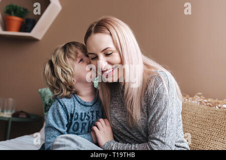 Sohn ist seiner Mutter küssen. Mutter und Sohn. Happy Mother's Day. Mutter ihr Kind zu Hause umarmen Stockfoto