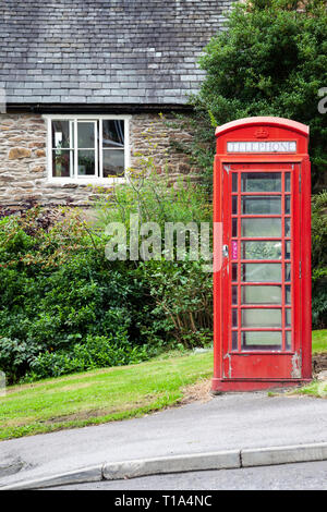 Ein Altmodisches Britisches Rotes Telefon" auf Weiter, um einen Pfad vor einem alten Haus aus Stein Stockfoto