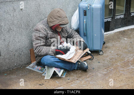 New York, NY - 12. Februar 2019: ein Obdachloser ist Essen, während Sie ein Zeichen für Hilfe, Essen und Geld. Midtown Manhattan. - Bild Stockfoto