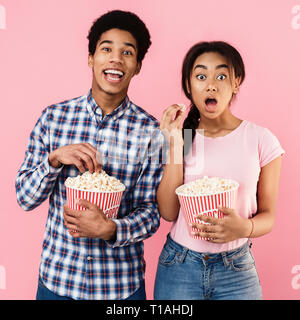 Schockiert Paar essen Popcorn über rosa Hintergrund Stockfoto