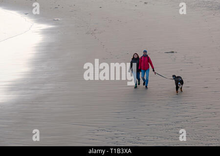 Bournemouth, Dorset, Großbritannien. 25. Mär 2019. UK Wetter: Nach einem schönen sonnigen Tag, der Tag endet mit einem goldenen Sonnenuntergang am Strand von Bournemouth, als Besucher der seaside Kopf die letzten Strahlen der Sonne zu genießen und die Sonne beobachten. Paar ihre Berner Sennenhund entlang der Küste. Stockfoto