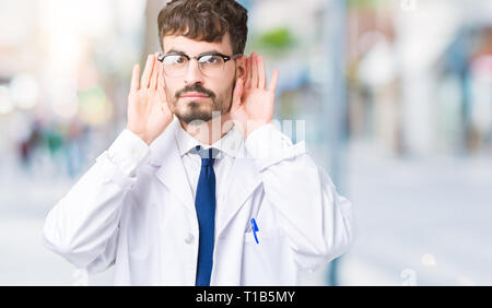Junge Wissenschaftler Mann mit weißer Mantel über isolierte Hintergrund versuchen, beide Hände am Ohr Geste zu hören, neugierig, für Klatsch und Tratsch. Anhörung pro Stockfoto