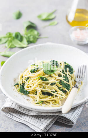 Spaghetti Pasta mit Spinat und grünen Pesto, in einer weißen Platte am grauen Stein Hintergrund Stockfoto