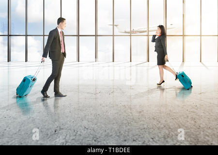 Attraktive zwei asiatische Geschäftsleute mit Handy und blauen Koffer auf dem Flughafen Halle mit Fenster aus Glas und fliegende Flugzeug über bl Stockfoto