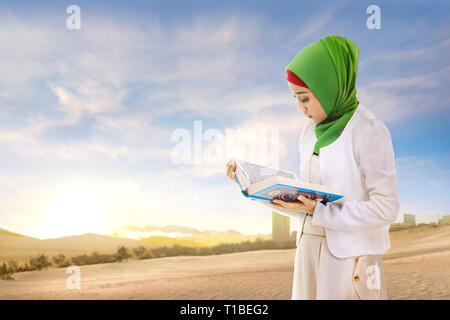 Schöne asiatische Muslimin in Schleier stehen und Lesen des Qur'an und der Sand mit blauem Himmel Hintergrund Stockfoto