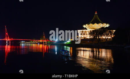 Malerische Nacht Blick auf den beleuchteten Zustand gesetzgebenden Versammlung und Fußgängerbrücke. Boot zu Fuß von Sarawak River. Sehenswürdigkeiten in Kota Kuching Waterfront. Stockfoto