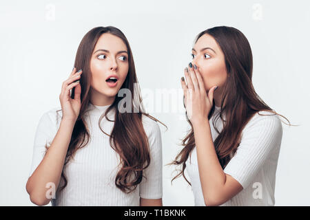 Zwei Schwestern, die Zwillinge klatschen auf weißem Hintergrund. Geheimnis für uns Konzept Stockfoto