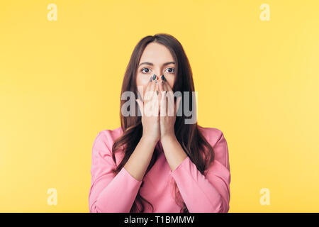 Schockiert begeistert Frau, die ihren Mund mit den Händen auf gelben Hintergrund isoliert Stockfoto