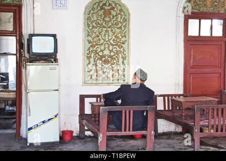 Uigurischer Mann beim Fernsehen in einem Teehaus in Kashgar, Autonome Region Xinjiang, China. Stockfoto