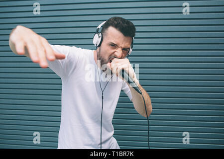 Cool und super Mann liest Rap in das Mikrofon. Er zeigt seine Hand und Kamera. Kerl singt, Mikrofon und Kopfhörer trägt. Isoliert Stockfoto