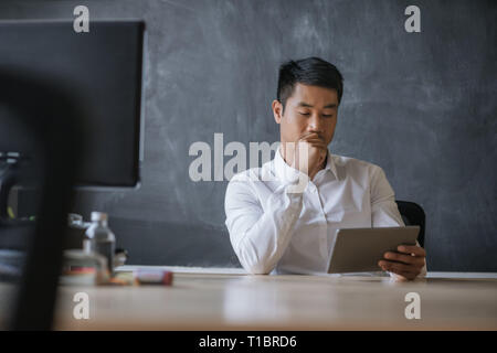 Asiatische Geschäftsmann an seinem Schreibtisch arbeiten auf einem Tablet sitzen Stockfoto