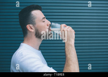 Ein Bild des Menschen trinken Milch aus Glas. Er hält die Augen geschlossen. Auf gestreifte und blauem Hintergrund isoliert. Stockfoto