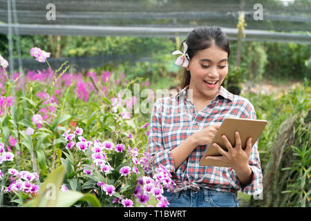 Weibliche Gärtner tragen Karohemden. Es gab Orchideen herauf die Ohren, die Hand mit der Tablette und Pointing Finger auf dem Tablett und lächelnd Stockfoto