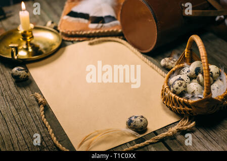 Vintage mock up. Closeup Körbchen mit Wachteleier neben Leuchter und gelbes Papier für Text auf rustikalen, mit Holz. Stockfoto