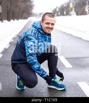 Lächelnd Mann binden Schnürsenkel auf Sneakers vor Ausführen Stockfoto