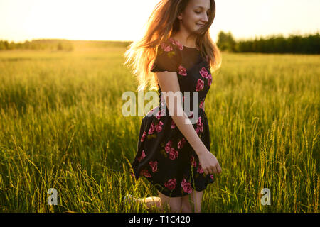 Junge Mädchen in Flower dress, Laufen oder Springen vom Glück auf der grünen Wiese. Sie lächelt und ihr langes Haar fließen auf Wind, alle von w leuchtet Stockfoto