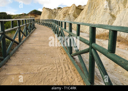 Holz-, grünen Fußgängerbrücke auf Dünen, zwischen Felsen und Sandstrand. Romantische Promenade für einen Spaziergang bei Sonnenuntergang im Sommer Urlaub in mediterran Stockfoto