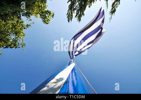 Große Griechenland Flagge weht im Wind, im Sommer täglich. Ansicht von unten auf der malerischen Moment der größten griechischen Flagge in der Welt, blauer Himmel und Bäume Stockfoto