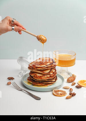 Frau giesst Honig auf Pfannkuchen. Das Konzept der ein leckeres Frühstück. Stockfoto