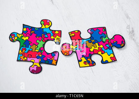 Zwei Puzzleteile mit vielen Puzzleteilen in verschiedenen Farben, Symbol der autism Bewußtsein, auf weißem Hintergrund rusitc Holzmöbeln gemusterten Stockfoto