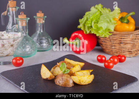 Hausgemachte gebackene organic Potato Wedges mit Kräutern auf einem Teller mit frischem Gemüse auf dem Hintergrund Stockfoto