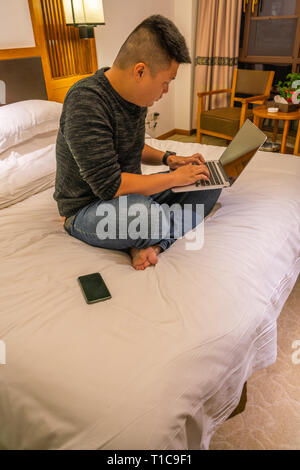 Junger Mann sitzt auf dem Bett und mit laptop Stockfoto