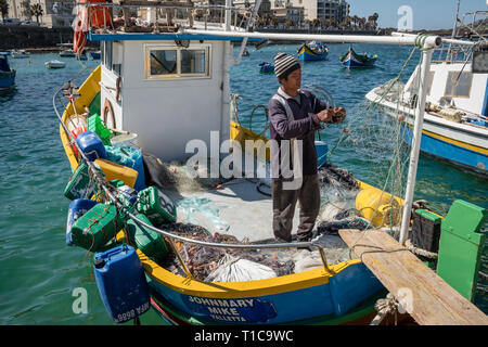 Ein Fischer Art seine Netze auf einem traditionellen Fischerboot bekannt als Luzzu, St. Paul's Bay, Malta Stockfoto