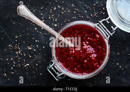 Hausgemachte Erdbeermarmelade mit Chia Samen in ein Glas mit einem Löffel im Inneren auf schwarzem Hintergrund. Gesunde Idee zum Frühstück Toast. Superfoods und gesunden fo Stockfoto