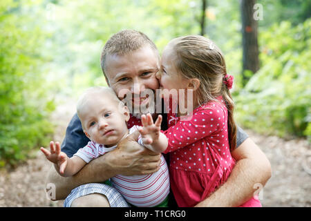 Vater seinen Sohn und Tochter umarmen gewidmet, genießen die outdoor. Familie Liebe und Bindung, aktiven Lebensstil, Vatertag Konzept. Stockfoto