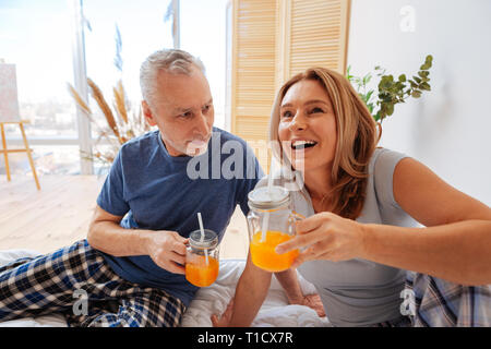 Mann und Frau tragen Schlafanzug Saft trinken im Schlafzimmer Stockfoto
