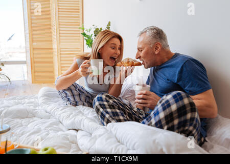 Liebevolle lustige Frau ihren Croissant gemeinsam mit ihrem Mann Stockfoto