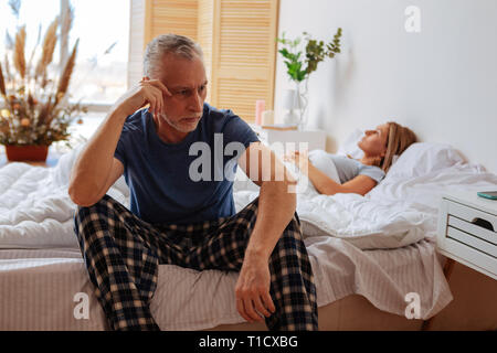 Grauhaarige Mann tragen Schlafanzug in der Nähe von Sleeping Frau sitzen Stockfoto