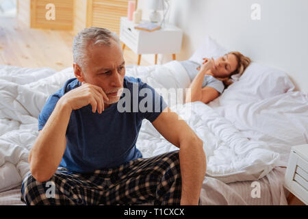 Betroffenen verärgerten Mann sitzen auf dem Bett in der Nähe von Sleeping Frau Stockfoto