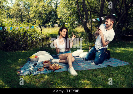 Junges Paar auf ein Picknick im Park sitzen auf einer Decke nimmt er ein Bild ihrer selektiven Fokus Stockfoto