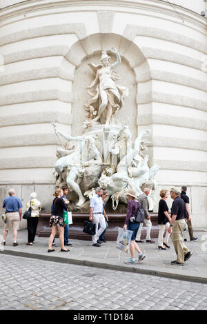 Touristische Spaziergang, vorbei an den Power auf See behauene Brunnen von Rudolf Weyr auf der Fassade der St. Michael's Flügel der Hofburg in Wien, Österreich.