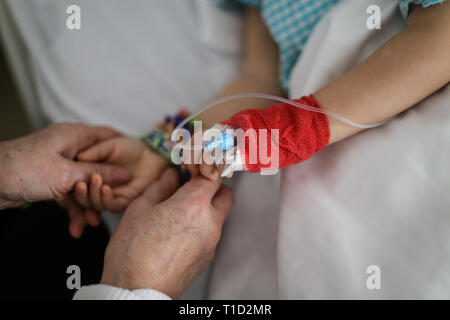 Details mit den Händen einer Großmutter trösten ihre Enkelin Wer hat eine Kanüle auf der Hand, in eine Kinderklinik finden Stockfoto