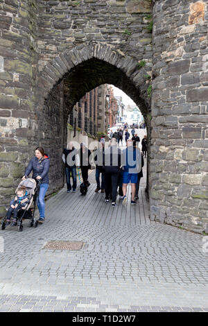 Touristen und Einheimischen, die durch die alte Mauer arch zu Conwy Kai im Norden von Wales, die vom Kai am Unteren Tor Straße zur High Street führt Stockfoto