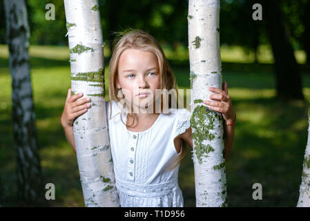 Portrait von schönen Mädchen in weißem Kleid umarmte Birke Stockfoto