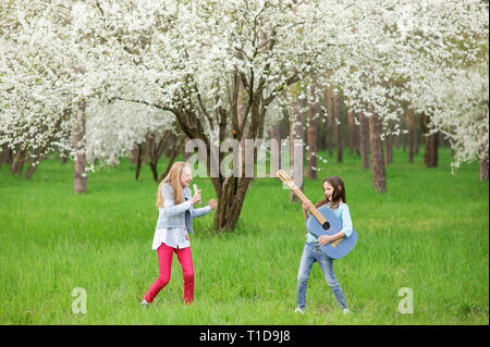 Kinder Rock Band von zwei lustige kleine Mädchen mit Vintage Gitarren und haarbürste als Mikrofon Musik spielen und singen Song im Frühjahr blühen Park Outdoor Stockfoto